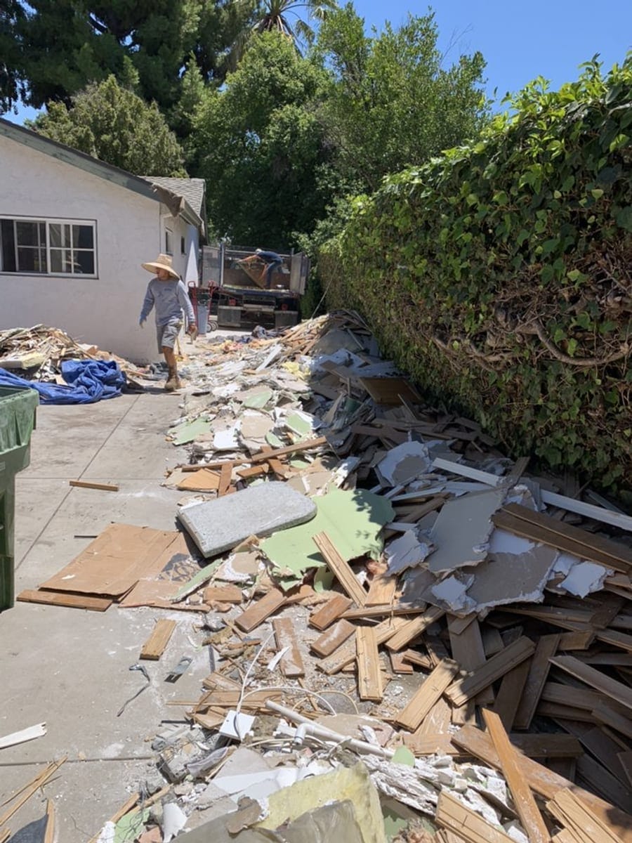 Junk removal worker clearing a pile of timber and household debris beside a Palm Bay home